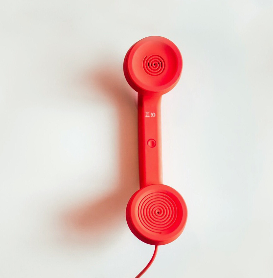 Roter Telefonhörer vor weißem Hintergrund.