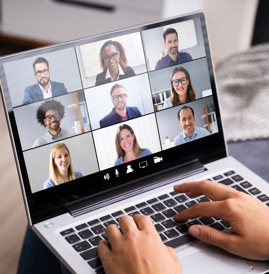Bildschirm mit neun Teilnehmenden einer Videokonferenz, davor zwei Hände auf der Tastatur.